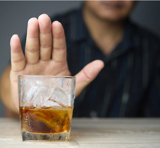 Мужчина протянул руку перед стаканом с алкоголем