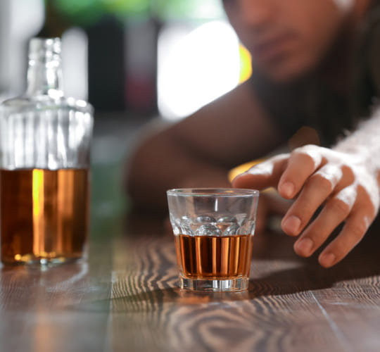 мужчина тянется к стакану с алкоголем